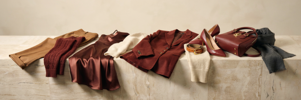 Capi e accessori bordeaux e cammello disposti in fila: cappotto, maglione, abito in raso, blazer, décolleté, borsa e sciarpa - come abbinare il bordeaux autunno 2026